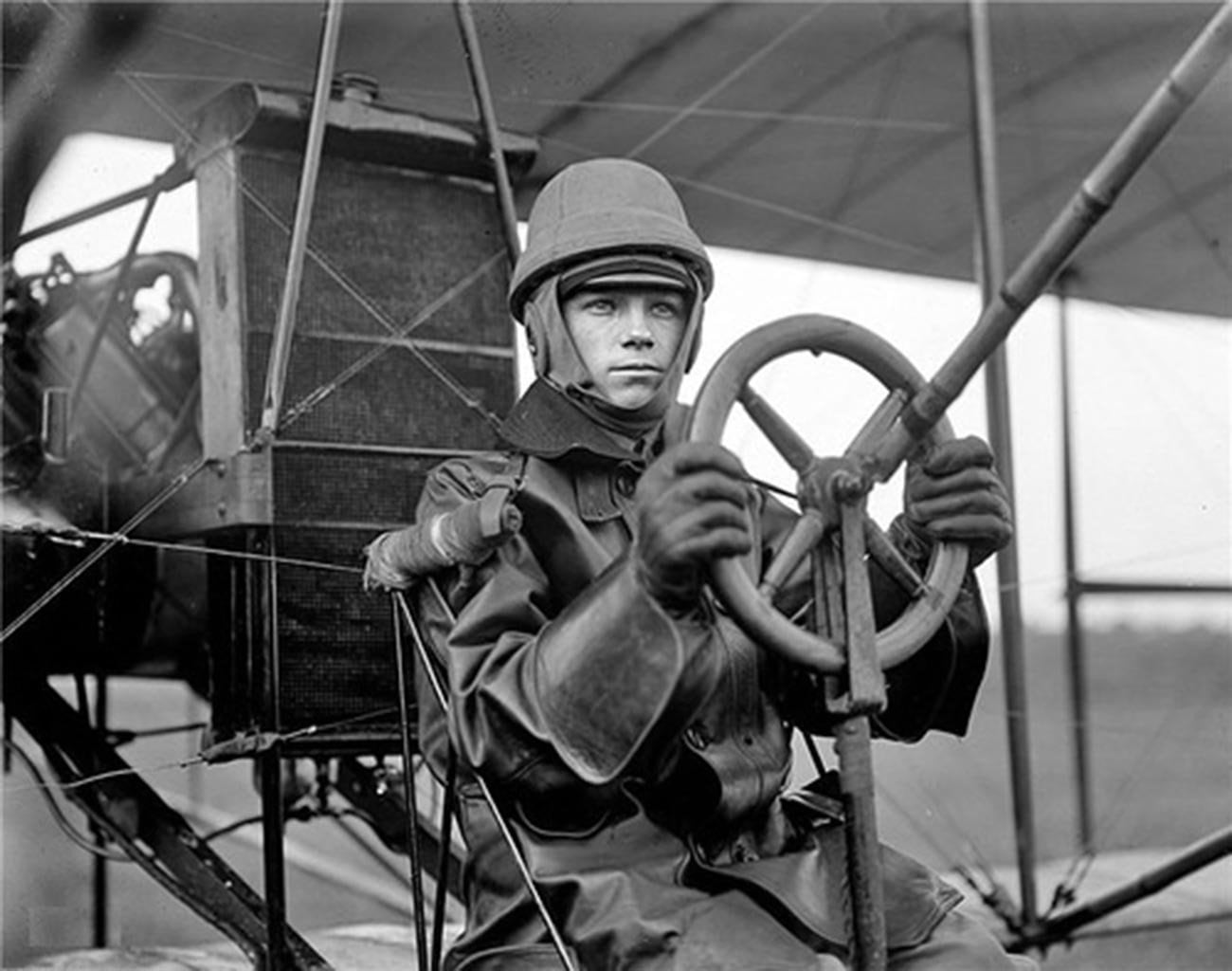 Early aviator in goggles at the controls of a vintage biplane
