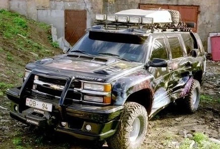 The black DARTZ Star Kombat SpaceBaller, with a roof rack of lamps and painted flanks, on rough ground